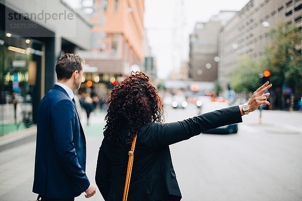 Businessman standing by businesswoman hailing taxi on street in city