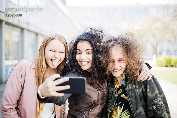 Happy teenage girl taking selfie with friends from smart phone