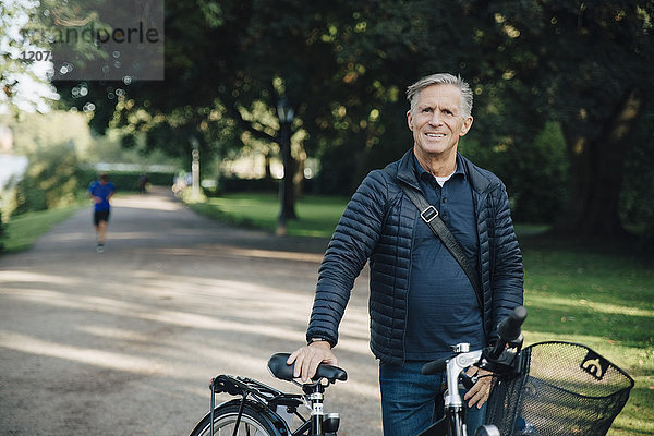Porträt eines lächelnden älteren Mannes mit einem Fahrrad im Park