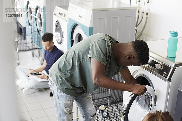 Mann mit Waschmaschine während des Studiums am Waschsalon