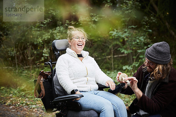 Fröhliche behinderte Frau im Rollstuhl von Hausmeisterin mit Pilz im Wald