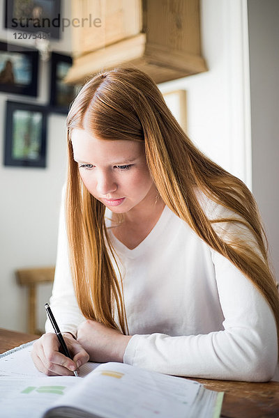 Blondes Mädchen lernt am Tisch  während es in einem Buch schreibt.