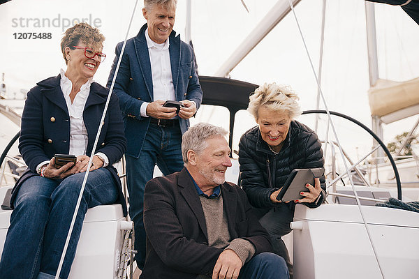 Seniorenpaar mit digitalem Tablett auf Reisen mit Freunden in der Yacht
