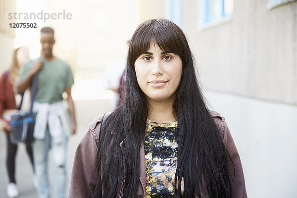 Porträt einer jungen Frau mit langen Haaren auf dem Universitätsgelände mit Freunden im Hintergrund