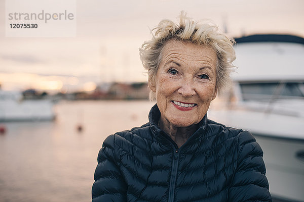 Porträt einer älteren Frau  die bei Sonnenuntergang im Hafen lächelt.