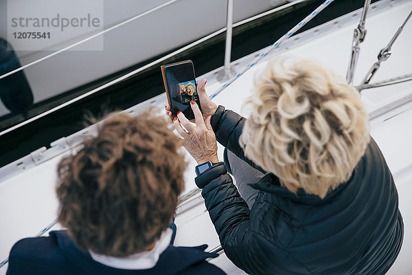 Hochwinkelansicht einer älteren Frau  die ein Foto auf dem Handy einer Freundin in der Yacht zeigt.