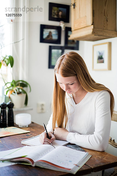 Blondes Mädchen schreibt im Buch  während es zu Hause sitzt