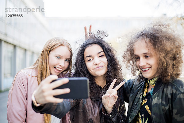 Lächelndes Teenager-Mädchen nimmt Selfie mit Freunden von Smartphone