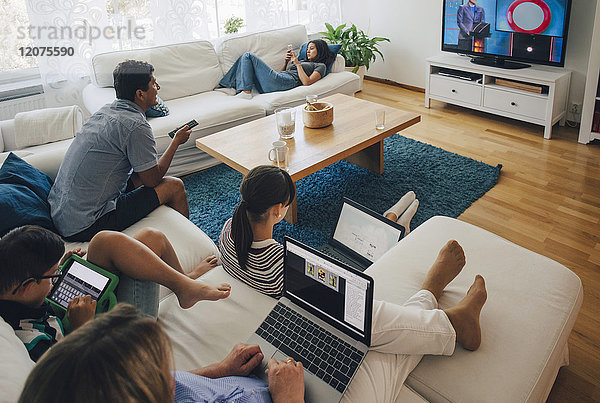 Hochwinkelansicht der Familie mit Hilfe von Technologien beim Entspannen im Wohnzimmer zu Hause