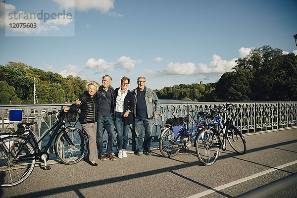 Volle Länge der älteren männlichen und weiblichen Freunde mit auf der Brücke stehenden Fahrrädern
