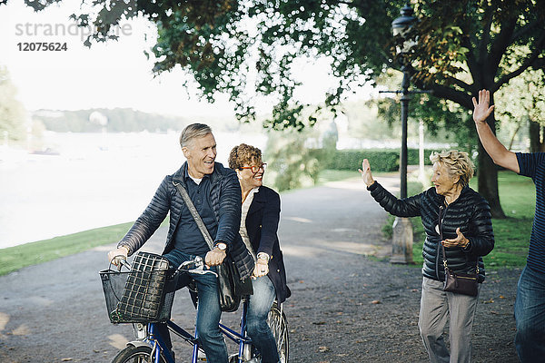 Seniorenpaar winkt mit Freunden auf dem Tandemfahrrad im Park