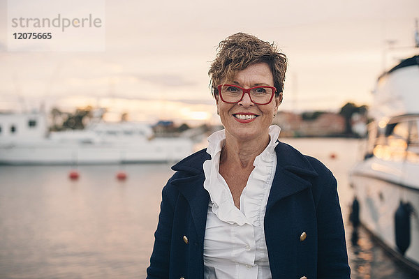 Porträt der lächelnden Seniorin im Hafen bei Sonnenuntergang