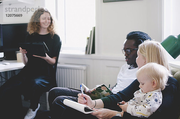 Arbeitende Mutter mit Baby diskutiert mit Kollegen im Kreativbüro