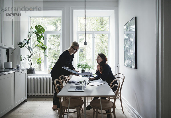 Weibliche Kollegen diskutieren über Dokument am Tisch im Home-Office