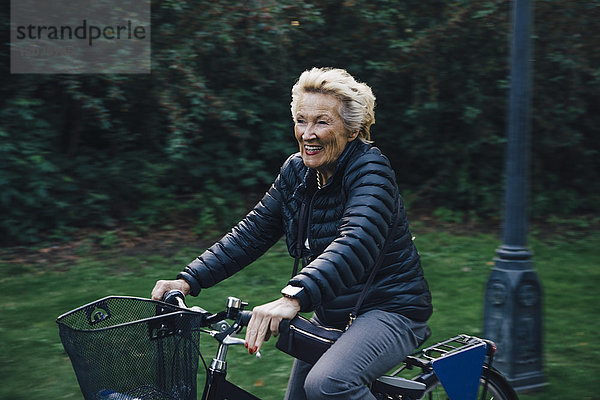 Lächelnde Seniorin beim Fahrradfahren im Park