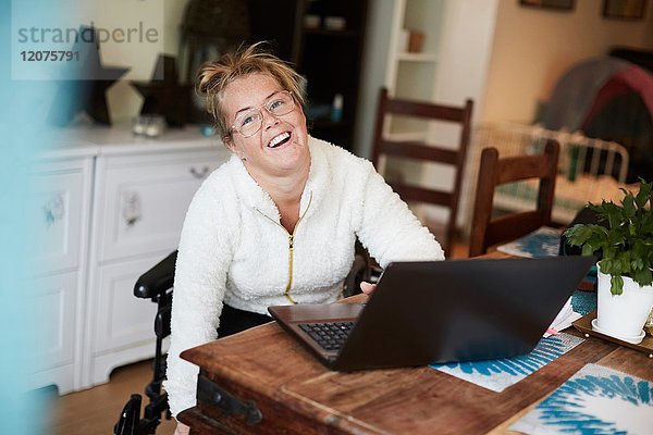 Porträt einer lächelnden behinderten Frau mit Laptop am Tisch im Haus