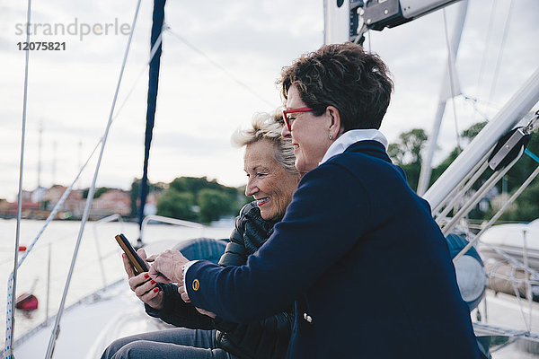 Lächelnde Seniorinnen mit Handy auf der Yacht