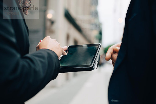 Mittelteil der Geschäftskollegen mit digitalem Tablett in der City