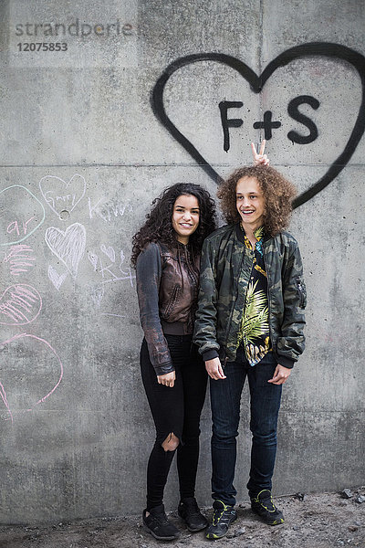 Fröhliche Teenager-Freunde stehen gegen Graffiti auf der grauen Wand in der Stadt.