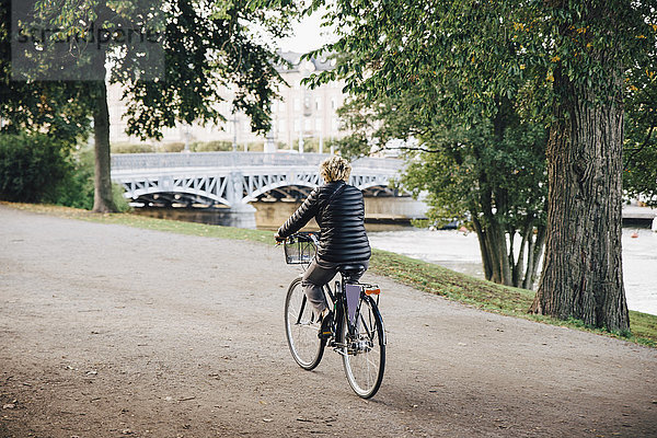 Durchgehende Rückansicht der Seniorin auf dem Fahrrad im Park