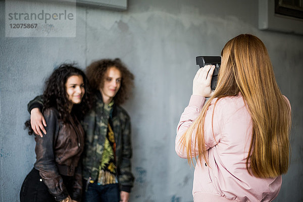 Rückansicht eines Mädchens  das Teenager-Freunde fotografiert  die an der Wand im Parkhaus stehen.