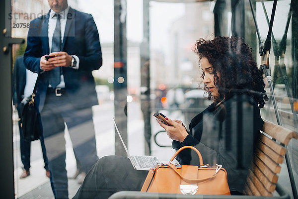 Geschäftsleute  die Smartphones benutzen  während sie in der Bushaltestelle warten.