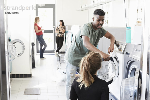 Universitätsstudentin im Gespräch mit der Frau an der Waschmaschine  während Freunde im Hintergrund stehen