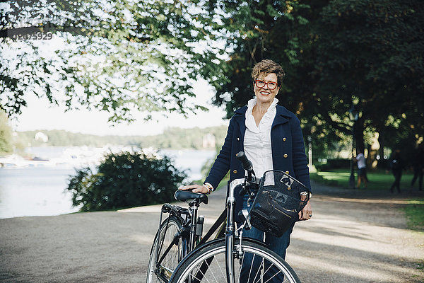 Porträt einer lächelnden Seniorin mit Fahrrad im Park