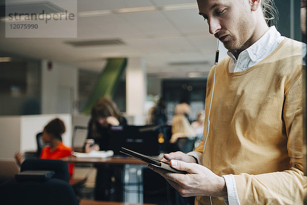Mittlerer erwachsener Geschäftsmann mit digitalem Tablett im Stehen im Büro