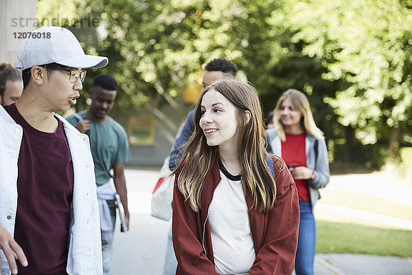 Lächelnde Freunde beim Spaziergang auf dem Uni-Campus an sonnigen Tagen
