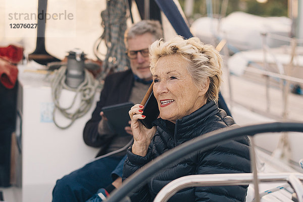 Seniorin spricht auf dem Handy  während sie von einem Mann auf einer Yacht sitzt.