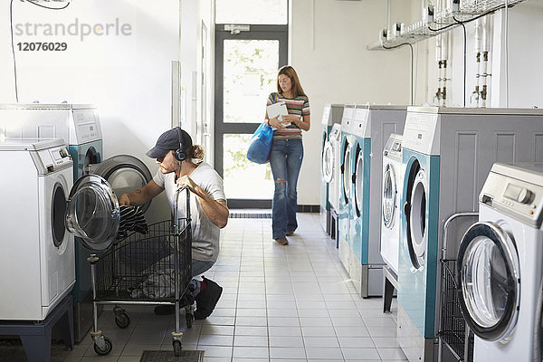 Mann mit Waschmaschine  während Frau im Waschsalon läuft