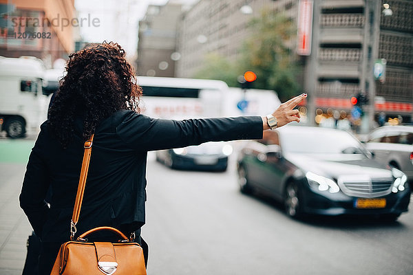 Rückansicht der mittleren erwachsenen Geschäftsfrau  die ein Taxi auf der Straße in der Stadt hagelt.