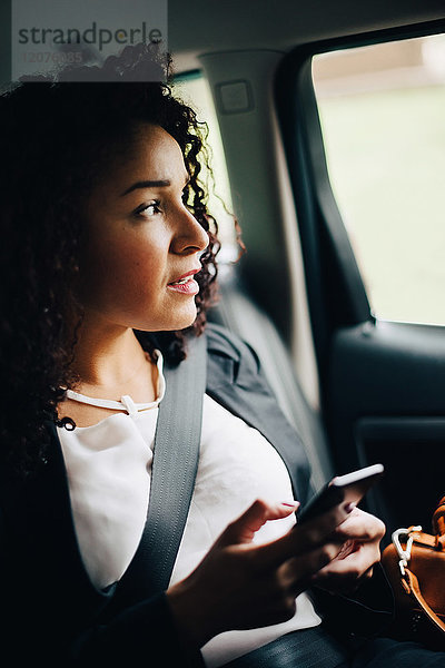 Mittlere erwachsene Geschäftsfrau beim Sitzen mit Smartphone im Taxi