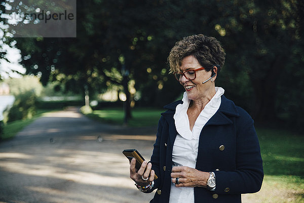 Seniorin mit Freisprecheinrichtung während der Benutzung des Mobiltelefons im Park