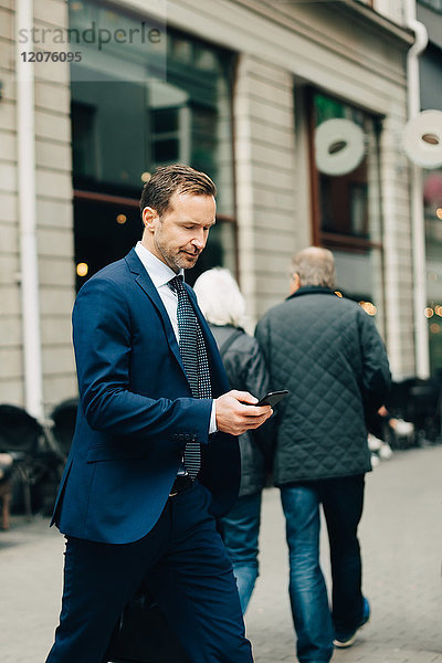 Reife Geschäftsleute mit Smartphone beim Gehen auf dem Bürgersteig in der Stadt