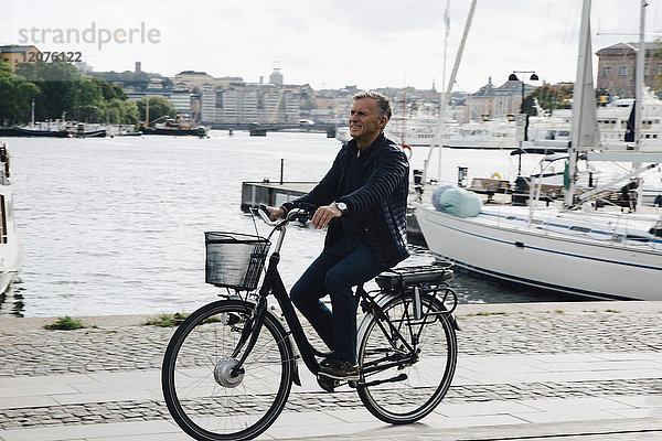 Volle Länge des älteren Mannes beim Radfahren auf der Straße am Hafen