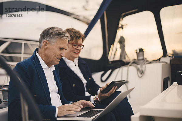 Seniorenpaar  das bei Sonnenuntergang in der Yacht unterwegs ist und Technologien einsetzt