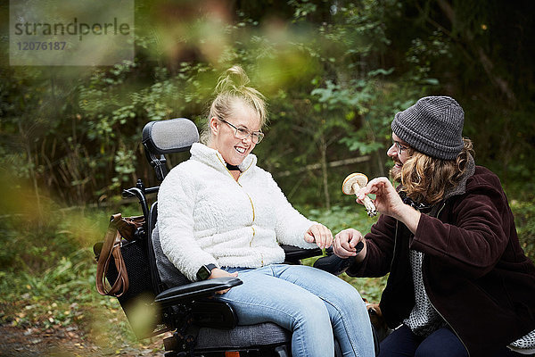Männlicher Hausmeister zeigt behinderten Frauen im Rollstuhl im Wald den Pilz