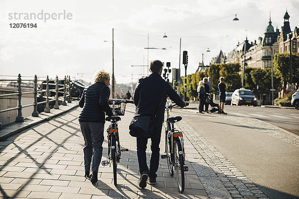 Durchgehende Rückansicht des Seniorenpaares mit Fahrrädern auf dem Bürgersteig in der Stadt
