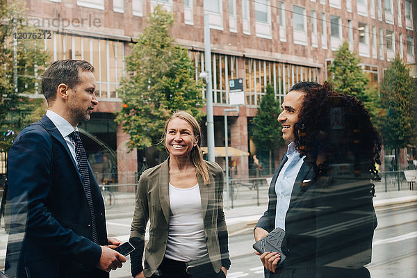 Lächelnde Geschäftskollegen diskutieren im Stehen auf der Straße vom Glas aus gesehen