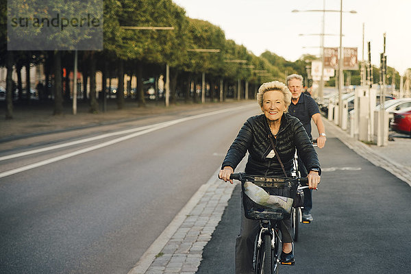 Porträt einer lächelnden Seniorin mit einem Mann  der auf der Stadtstraße Fahrrad fährt