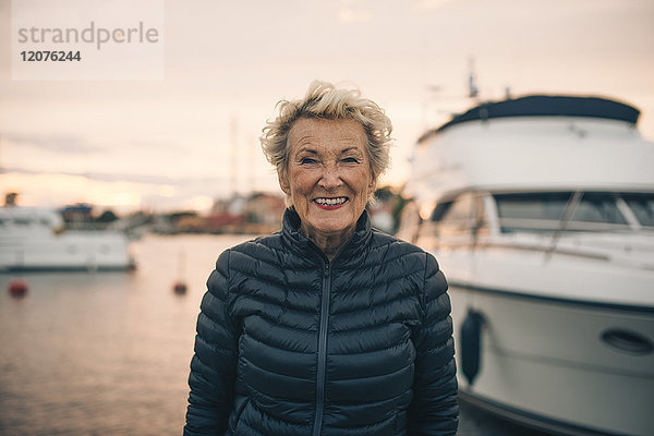 Porträt einer glücklichen älteren Frau  die bei Sonnenuntergang am Hafen steht.