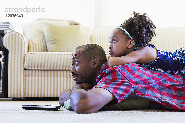 Gemischtrassiger Vater und Tochter liegen auf dem Boden und sehen fern