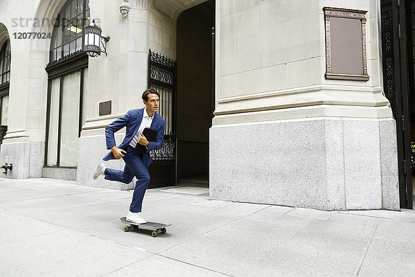 Kaukasischer Geschäftsmann  der auf einem städtischen Bürgersteig Skateboard fährt
