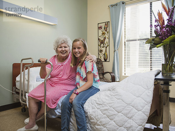 Lächelnde kaukasische Frau sitzt mit ihrer Enkelin auf dem Bett