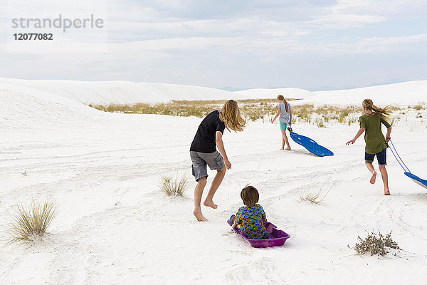 Kaukasische Jungen und Mädchen spielen auf Schlitten im Sand