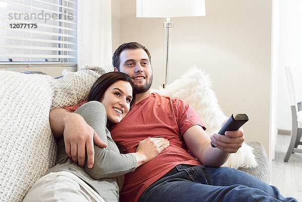 Kaukasisches Paar kuschelt auf dem Sofa und sieht fern