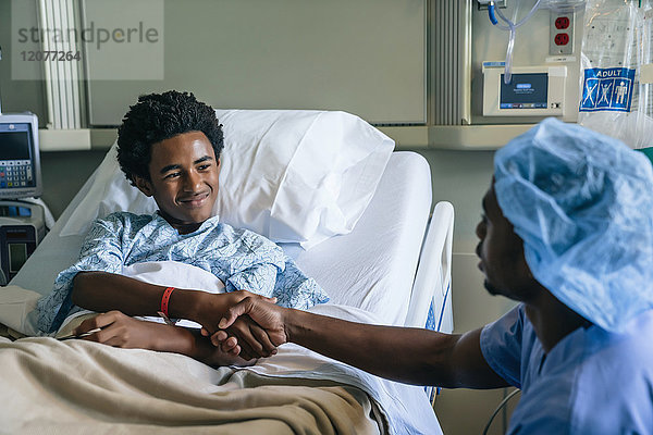 Schwarze Krankenschwester schüttelt dem Jungen im Krankenhausbett die Hand