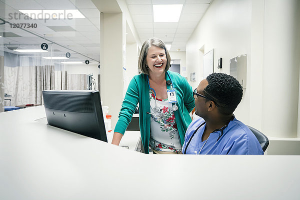 Arzt und Krankenschwester lachen neben dem Computer
